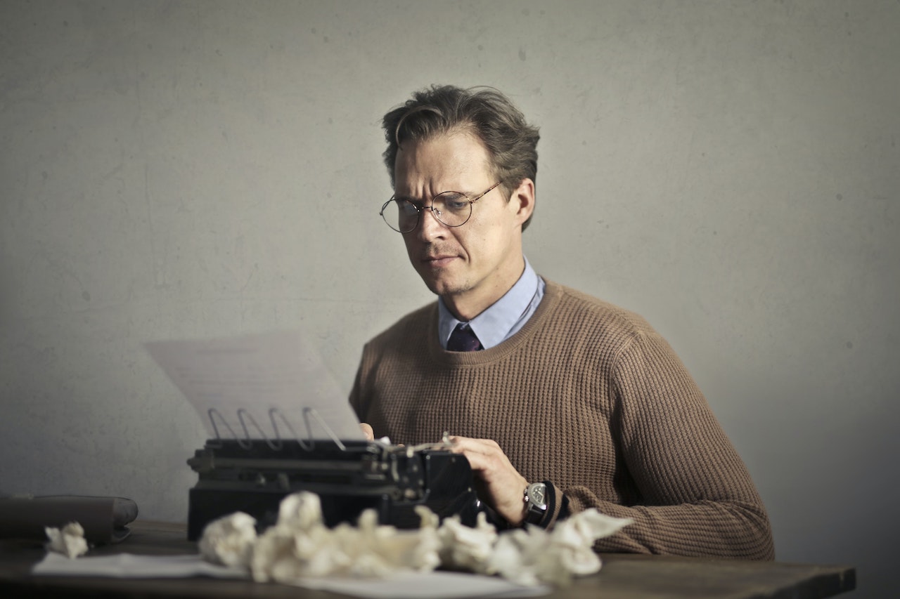 Man in a shirt, tie and brown sweater at a typewriter