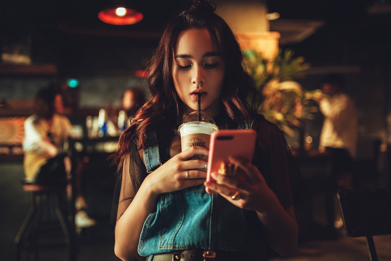 Woman drinking coffee reading content on her phone