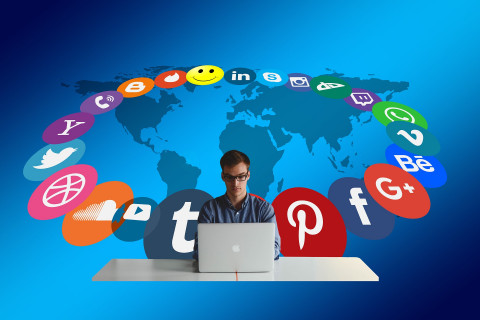 Social media icons swirling round a man using a laptop